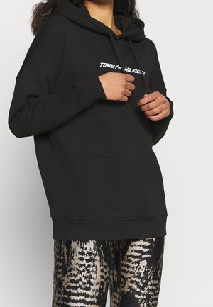 Felpa nera con cappuccio e tasca frontale, con il testo bianco "TOMMY HILFIGER". Abbinate a leggings lucidi con motivo a serpente.