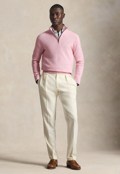 Ροζ ανοιχτόχρωμο πλεκτό πουλόβερ με φερμουάρ στο γιακά, συνδυασμένο με κρεμ ψηλόμεσα παντελόνια και καφέ μοκασίνια, δημιουργώντας μια κλασική εμφάνιση.