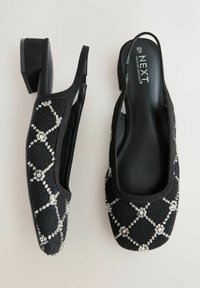 Sorte slingback-sko med en lav hæl, der har en struktureret stofoverflade med sølvfarvede palietter i diamantmønster og en rund tå.