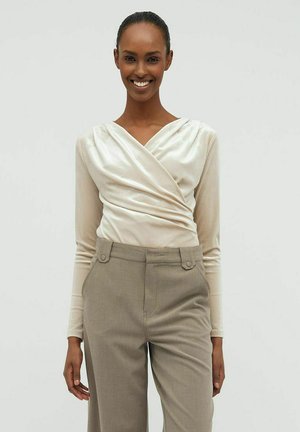 Beige indpakningsbluse med lange ærmer og glat, blank tekstur, parret med lysegrå højtaljede bukser med to frontknapper.