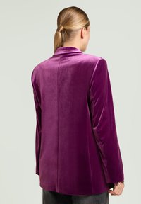 Blazer de terciopelo púrpura con cierre de un solo botón, solapas con muesca y mangas largas. Textura suave con un ajuste elegante.