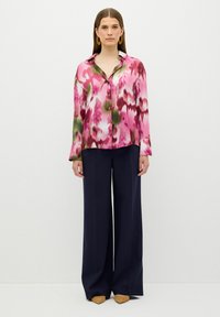 Blusa de patrón rosa y verde con botones, mangas largas y cuello, combinada con pantalones anchos azul marino y zapatos de tacón color caramelo.