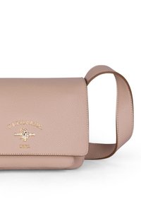 Beige läder axelväska med strukturerad yta, guldiga logotypdetaljer och en platt rektangulär form. Har en justerbar rem.