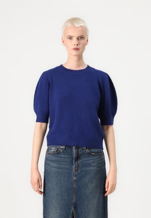 Pull court bleu royal à manches courtes avec un col rond et des manches bouffantes, associé à une jupe en denim avec une fente sur le devant et une coupe classique.