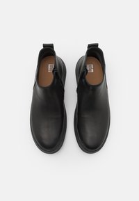 Sorte ankelstøvler laget av glatt lær med rund tå, sidelommer og en flat gummisåle. Enkel design med minimale detaljer.