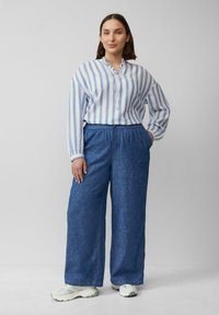 Blauw-witte gestreepte blouse met lange mouwen en een ruches kraag, gecombineerd met brede blauwe broeken en lichte sneakers.