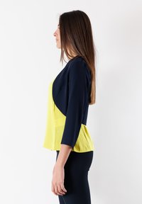 Blusa con un corpetto blu navy e un peplum giallo brillante, con maniche a tre quarti e un design in tessuto leggero e fluido.