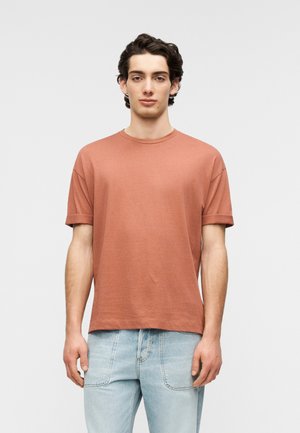 Kurzärmliges Hemd in Rostfarbe, aus weichem Stoff, mit Rundhalsausschnitt und lässiger Passform, kombiniert mit hellblauen Jeans.