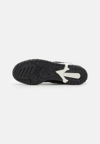 Suola di scarpa sportiva nera con grip in gomma testurizzata, un accento bianco stampato e un logo dal design circolare.