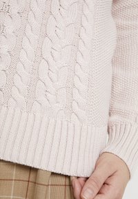 Rosa kabelstickad tröja med ribbat nederkant och ärmar, med texturerade mönster och en mjuk, mysig finish.