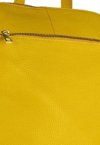 Detail van een gele leren tas met een gestructureerd oppervlak, gouden rits hardware en zichtbare stiksels langs de rand.