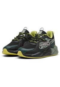 Chaussures de sport noires avec accents verts, dessus en maille, semelle texturée et lacets à motifs. Présente un logo sur le côté et des boucles au talon.