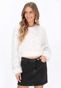 Valkoinen pörröinen lyhyt neule, jossa on monivärisiä pilkkuja ja ribbireunus; yhdistetty korkeavyötäröiseen mustaan farkkuhameeseen. Sujuva rakenne ja rento istuvuus.