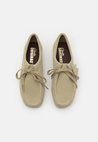 Scarpe in suede beige con chiusura allacciata, punta rotonda e cuciture crema. All'interno hanno una soletta marrone scuro con marchio "Clarks Originals".