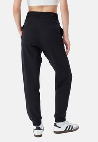 Schwarze Jogginghosen mit einem gerafften Bund, elastischen Bündchen, Seitentaschen und einer glatten Textur, kombiniert mit weißen Sneakers.