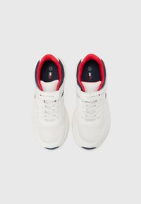 Baltos spalvos tinklelio sportbačiai su tekstūruota paviršiaus struktūra, tamsiai mėlynomis detalėmis ir raudonu pamušalu. Turi lipnią juostelę ir prekės ženklo liežuvėlio detalę.