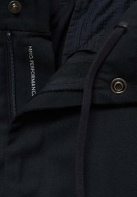 Čierna vonkajšia bunda s hladkou textúrou, ktorá má zipsovú kapsu, zapínanie na cvoky a detail s logom na vnútornom materiáli.