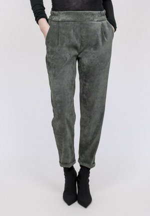 Personne portant un pantalon gris texturé à jambes fuselées avec les revers roulés, les mains dans les poches, associé à des bottines noires à bout pointu.