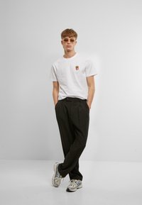 Hvid bomulds t-shirt med en farverig grafisk fries, parret med sorte brede bukser og grå sneakers, båret med lyse solbriller.