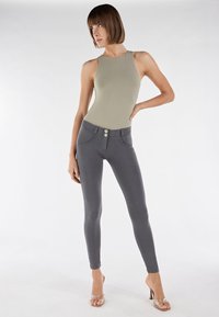  oliivinvihreä body korkealla kaula-aukolla, yhdistetty harmaisiin leggingsseihin, joissa on kaksi etunappia ja sileä pinta. Kirkkaakorkoiset sandaalit.