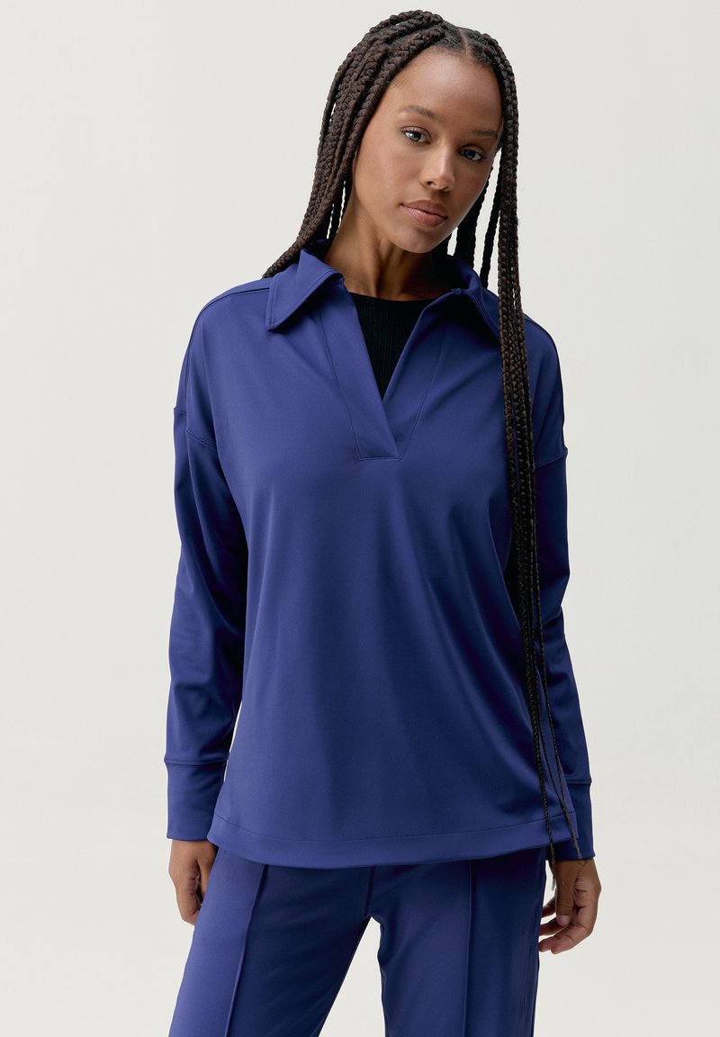 Pulovr s dlouhým rukávem v tmavě námořnické modři, s límcem a volným střihem. Vyrobeno z hladkého, lehkého materiálu.