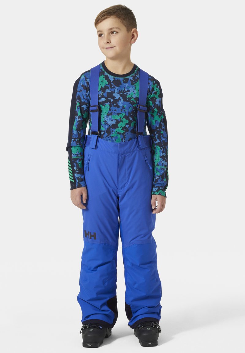 Blauwe skibroek met verstelbare bandjes, ritszakken en een zwart logo. Draag over een zwart en groen gestreepte basislaag met lange mouwen.