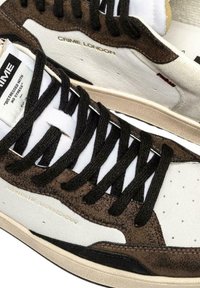 Sneaker basse bianche e marroni con lacci neri, marchio "CRIME LONDON" e etichetta "DISTRESSED WITH NO STRESS" sulla linguetta.