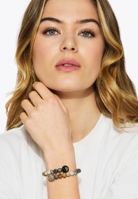 Bracciale in perline con tonalità di nero, argento e oro con accenti di cristallo, posato su uno sfondo chiaro e indossato al polso.