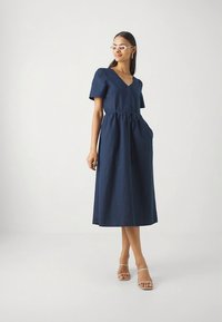 Vestido de linho azul-marinho com mangas curtas, decote em V, botões frontais, cintura franzida e bolsos laterais, com comprimento até ao meio da canela.