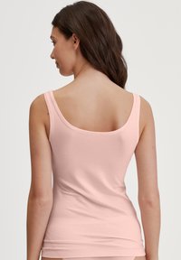 Pink tank top with a scoop neckline and narrow straps, made from a soft, stretchy fabric, featuring a fitted cut and smooth texture.