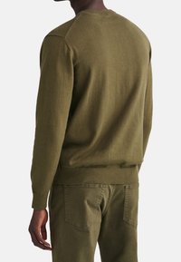 Olivgrüner gestrickter Pullover mit Rundhalsausschnitt und geripptem Saum. Besitzt eine glatte Textur und enganliegende lange Ärmel, kombiniert mit passenden Hosen.
