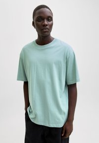 Miętowa bawełniana koszulka z krótkim rękawem, luźnym krojem i okrągłym dekoltem. Charakteryzuje się gładką fakturą i minimalistycznym wzornictwem.