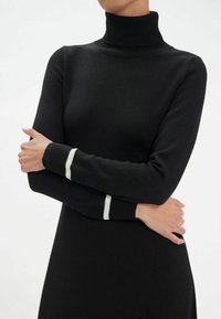 Robe noire à col roulé avec des manches longues, présentant des accents rayés blancs au niveau des poignets. Confectionnée dans un tissu lisse avec un design ajusté.