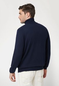 Maglione a collo alto lavorato a maglia blu navy con maniche lunghe, colletto e orlo a coste, caratterizzato da una texture liscia e dettagli sottili sulle spalle.