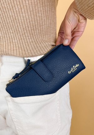 Navy blue leather wallet with a textured finish, zip closure, and a snap button. Features gold logo and fits in a pocket.