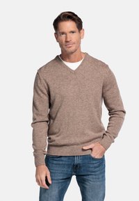 Lichtbruine V-hals trui van een zachte gebreide stof, gecombineerd met blauwe jeans. De trui heeft ribgebreide manchetten en een ribgebreide zoom.