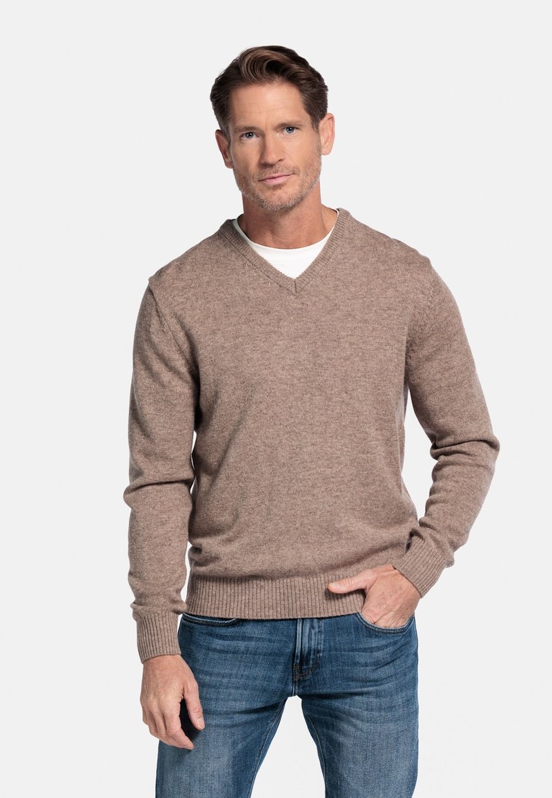 Lichtbruine V-hals trui van een zachte gebreide stof, gecombineerd met blauwe jeans. De trui heeft ribgebreide manchetten en een ribgebreide zoom.