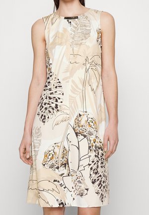 Robe beige sans manches avec motif feuilles tropicales et imprimé léopard portée par une femme debout.
