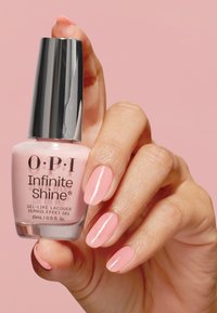 Lacca per unghie O.P.I. Infinite Shine in una tonalità rosa chiaro (15 ml) tenuta da una mano, con un tappo argentato lucido e finitura liscia sulle unghie.