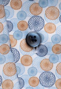 Katoenen stof met een witte achtergrond en complexe cirkelpatronen in blauw, oranje en bruin, verfraaid met een donkere knop.