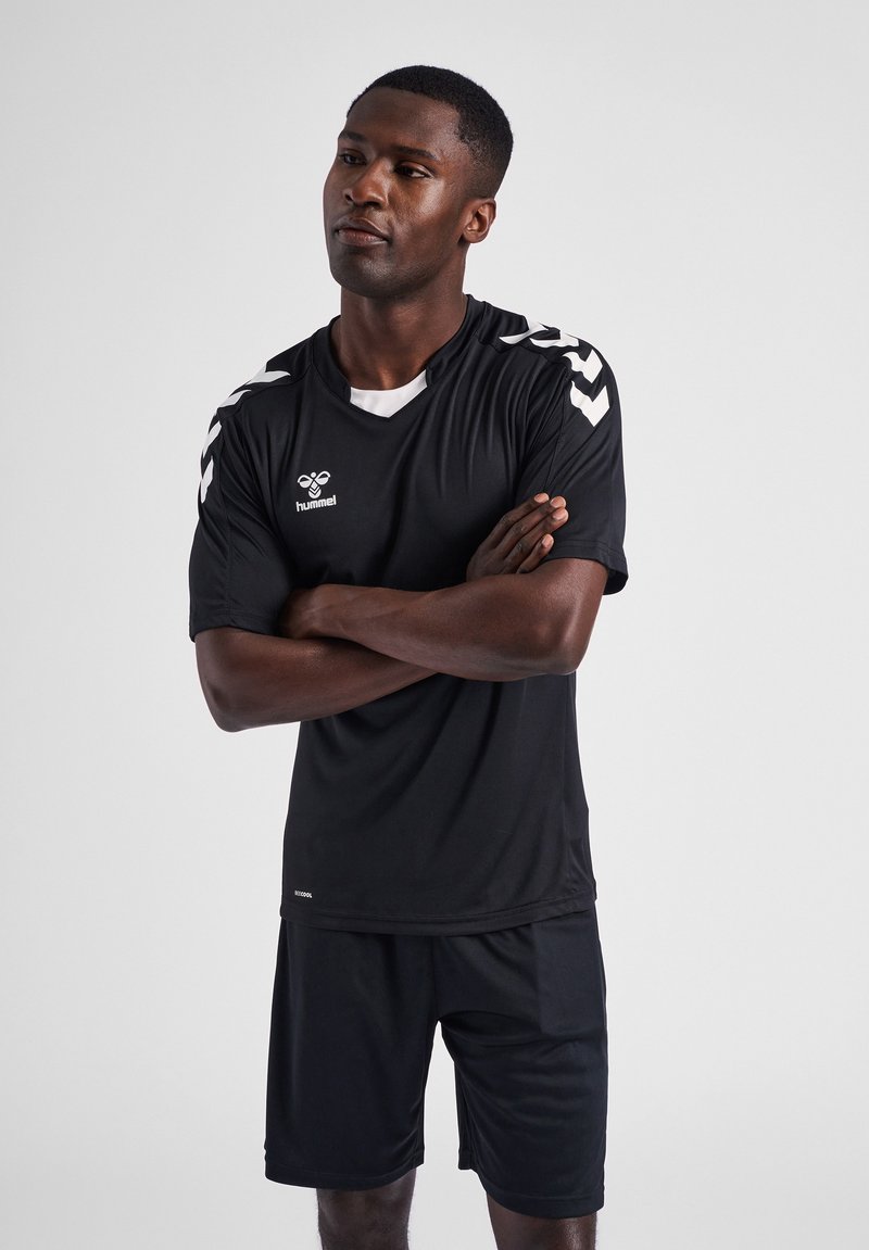 Zwart sportshirt en shorts gemaakt van ademend materiaal. Bevat witte chevronaccenten op de mouwen en een ronde halslijn.