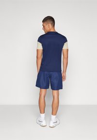 Navy blue sports shirt with light beige sleeves, paired with matching navy shorts. Fabric appears lightweight with a smooth texture.