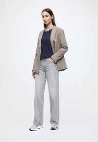 Hnedo-biela kockovaná sako cez námornícky modré tričko, v kombinácii so svetlošedými voľnými džínsami a sivými teniskami s bielymi akcentmi.