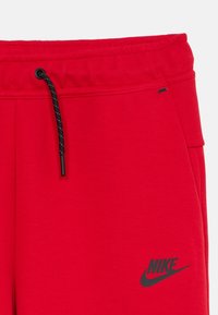 Červené športové tepláky s elastickým pásom, čiernym šnúrkou na stiahnutie a čiernym logom Nike na ľavom stehne. Hladká, priedušná tkanina.