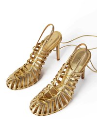 Sandale cu toc înalt, metalizate aurii, cu un design cu vârf deschis, având bretele crisscross și o curea subțire la gleznă. Textură netedă, structură elegantă.