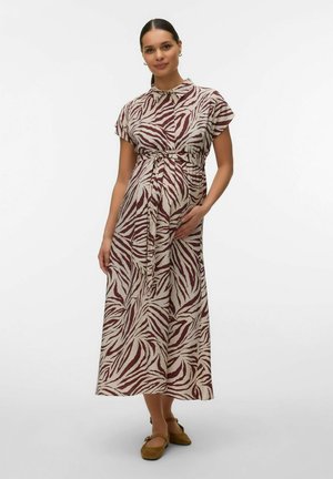 Mujer embarazada con un vestido midi de manga corta y botones, con estampado de cebra y cinturón de lazo, de pie con una mano sobre su vientre.