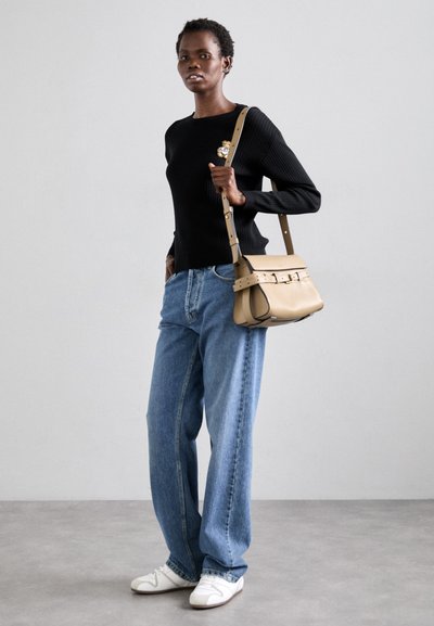 Black ribbed long-sleeve top features a small embroidered design. Light blue loose-fit jeans and a beige crossbody bag with straps. White sneakers.