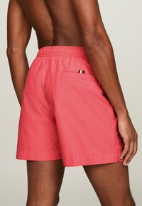 Bañador rosa con cinturilla elástica, bolsillo trasero y una pequeña etiqueta de tres colores. Tela suave con un diseño ligero.