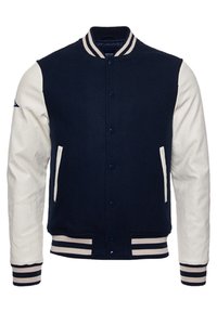 Marinblå ull varsityjacka med vita lädersärmar, ribbade muddar och krage med ränder, samt knappslutning. Har sidfickor.