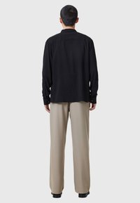 Zwarte lange mouwen shirt met geknoopte manchetten, gecombineerd met lichtbeige wijde broek en zwarte schoenen. De stof lijkt glad en licht van gewicht.